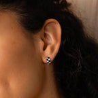 A close-up of an ear wearing Checkered Huggies—black and white hoop earrings with a trendy checkerboard design.