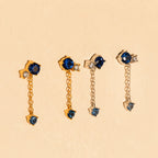 The Sapphire Diamond Drop Earrings feature blue and clear stones set in gold and silver, displayed on a beige background.