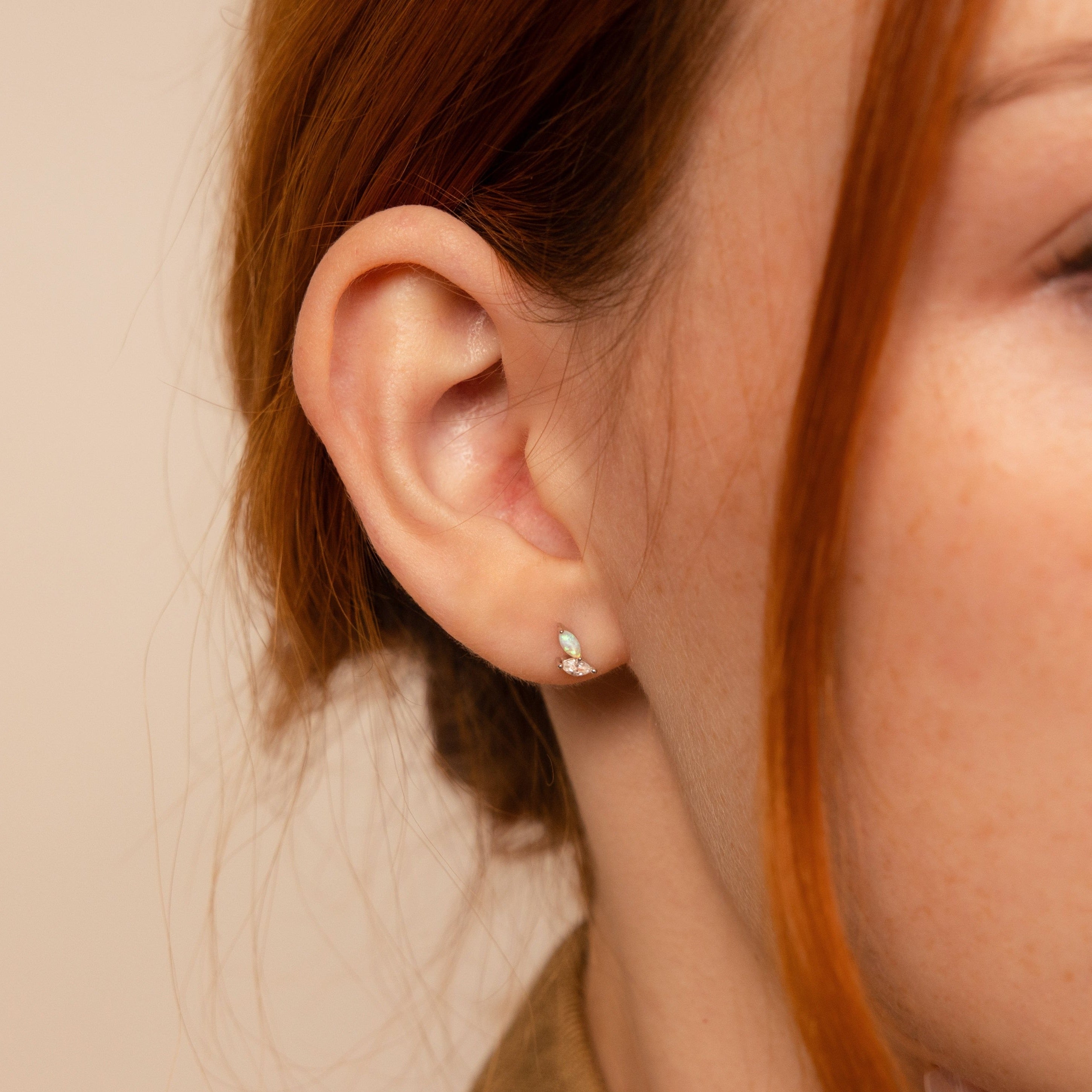 A close-up of a woman's ear wearing Opal & Diamond Marquise Studs, with strands of red hair visible—these elegant earrings make a timeless bridesmaid gift.