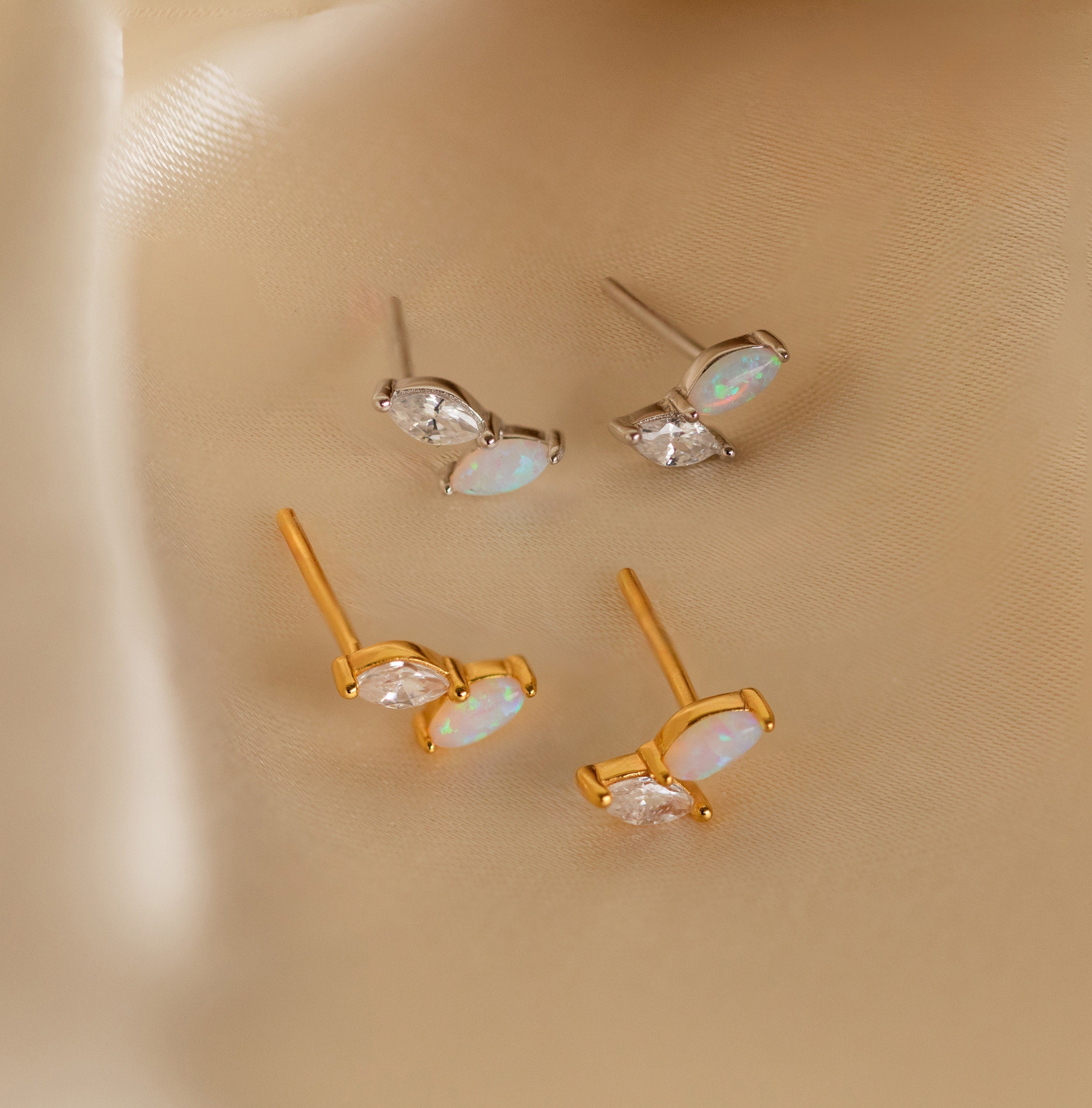 Two pairs of Opal & Diamond Marquise Studs, in gold and silver, displayed on silky beige fabric—ideal as a unique bridesmaid gift or for fans of mismatched earrings.