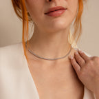 A woman in a white top touches her collarbone while wearing the Diamond Bezel Tennis Necklace—an elegant bridal accessory and the perfect gift for any bride.