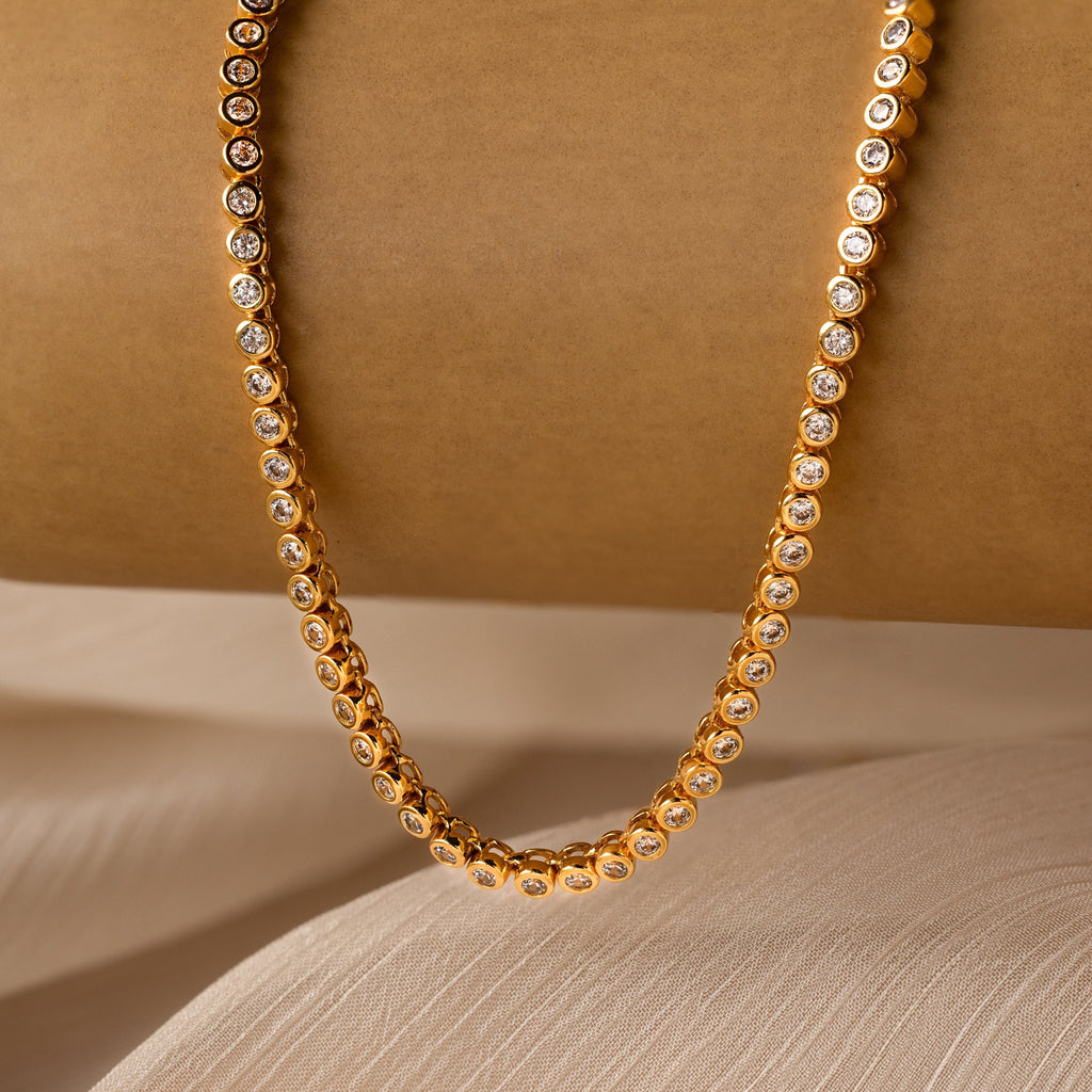 Diamond Bezel Tennis Necklace featuring round clear gemstones, elegantly displayed on a brown background with fabric underneath—a stunning bridal accessory and the perfect gift for any bride.