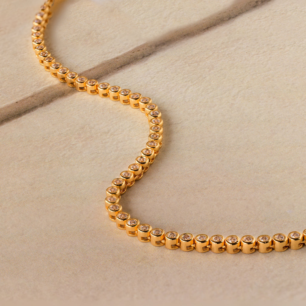 Diamond Bezel Tennis Necklace with round diamonds displayed on a beige stone surface—a stunning bridal necklace and a sophisticated gift for the bride.