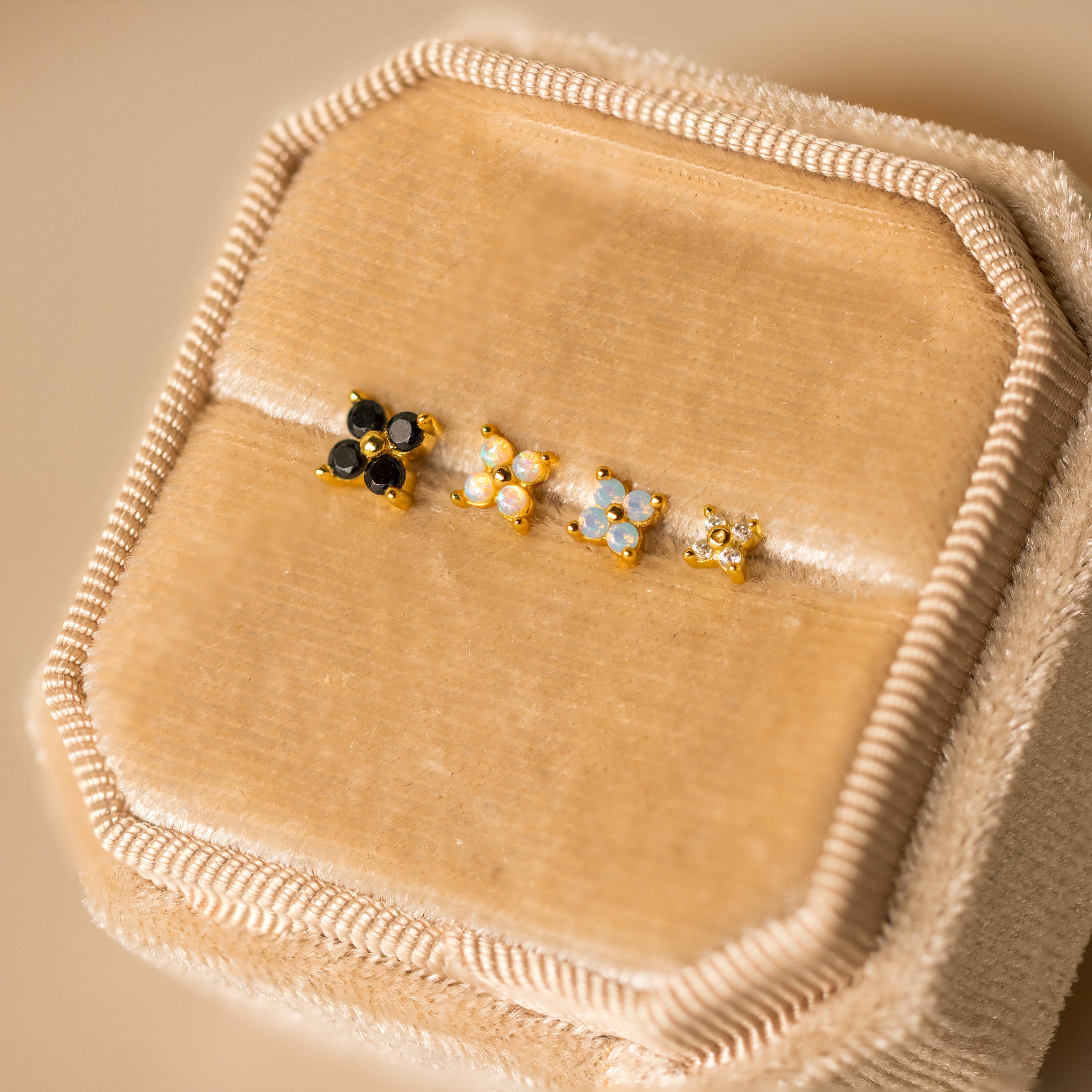 Four Opal Ivy Flower Studs with gold settings and colorful opal stones are displayed on a beige velvet jewelry box—an elegant, meaningful gift.