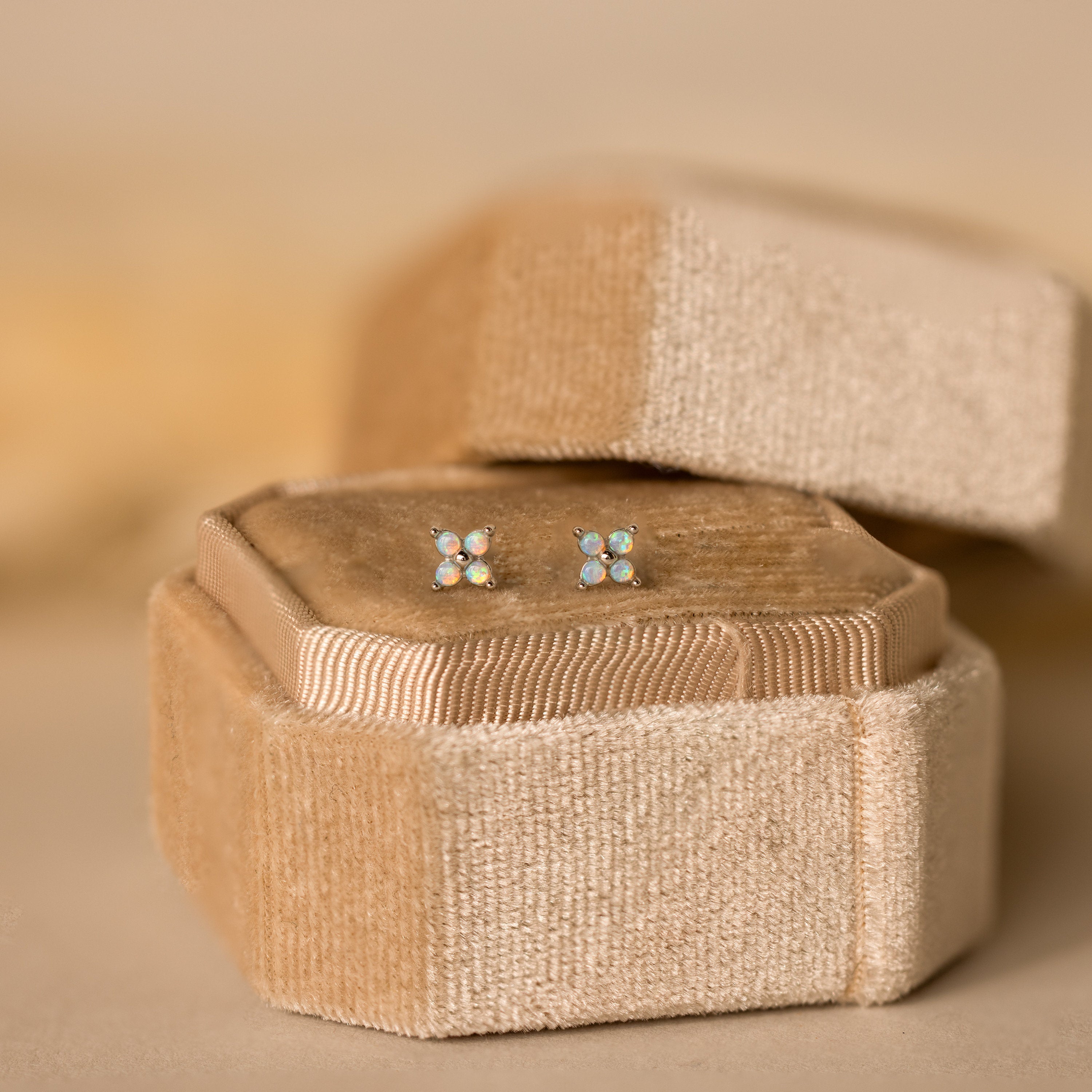 The Opal Ivy Flower Studs shimmer atop a beige velvet jewelry box with a gentle backdrop, making these earrings a thoughtful gift.