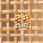 Two pairs of Opal Ivy Flower Studs, one gold and one silver, rest on a woven beige surface—beautiful earrings that make a meaningful gift.