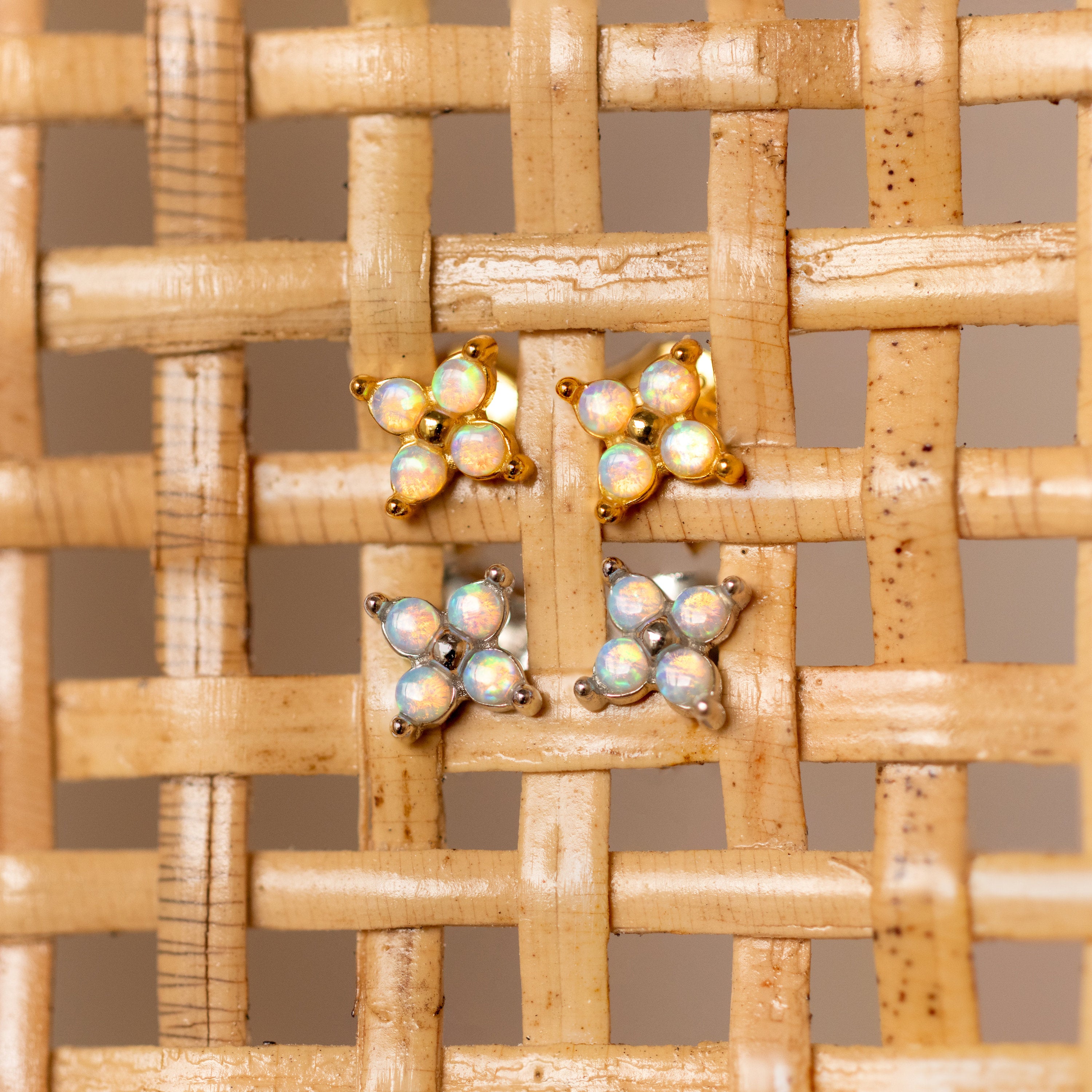 Two pairs of Opal Ivy Flower Studs, one gold and one silver, rest on a woven beige surface—beautiful earrings that make a meaningful gift.