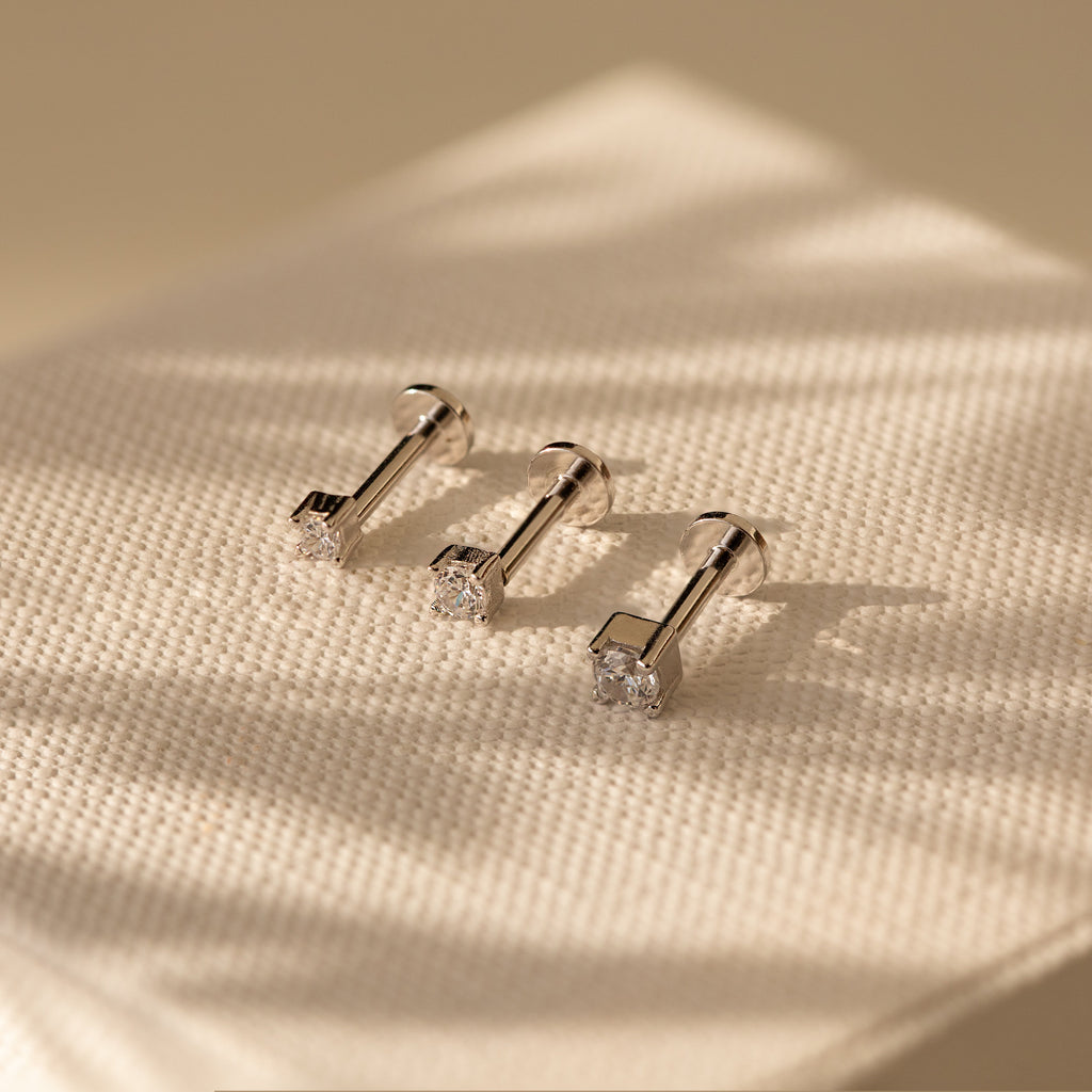 Three Diamond Flatback Studs Set in Sterling Silver, featuring clear gemstones, are displayed on textured cream fabric under soft light.