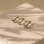 Three Diamond Flatback Studs Set in Sterling Silver, featuring clear gemstones, are displayed on textured cream fabric under soft light.