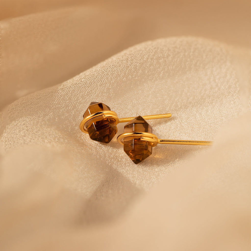 Herkimer Smoky Quartz Studs in gold and brown tones rest elegantly on soft, beige fabric.