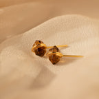 Herkimer Smoky Quartz Studs in gold and brown tones rest elegantly on soft, beige fabric.