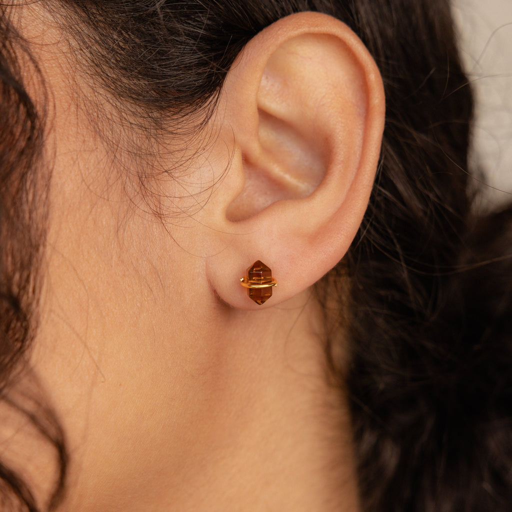 Close-up of a woman's ear wearing Herkimer Smoky Quartz Studs—small, gold and brown geometric stud earrings.