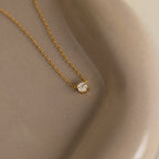 The Hexagon Diamond Necklace features a gold chain with a single rose-cut diamond pendant, showcased on a smooth beige ceramic dish.