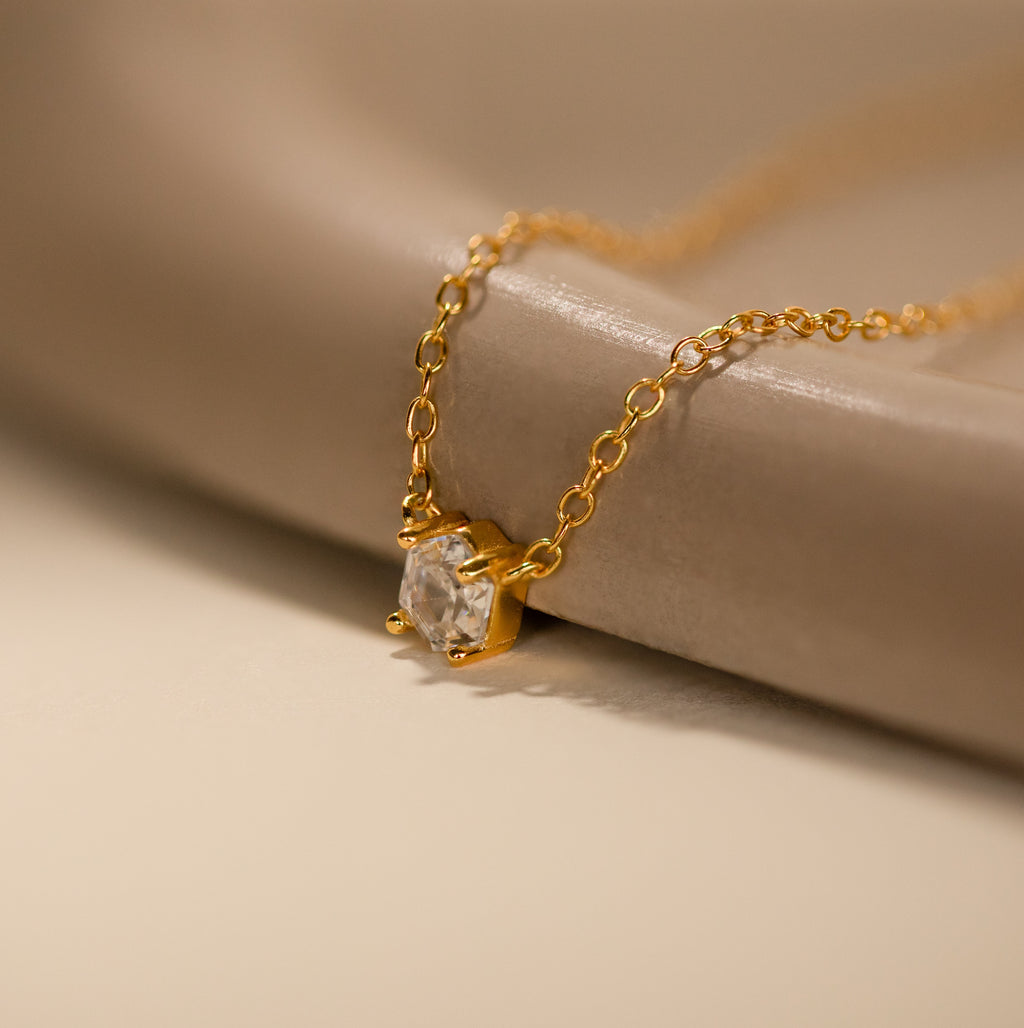 Hexagon Diamond Necklace featuring a rose-cut diamond pendant showcased on a smooth, beige surface.