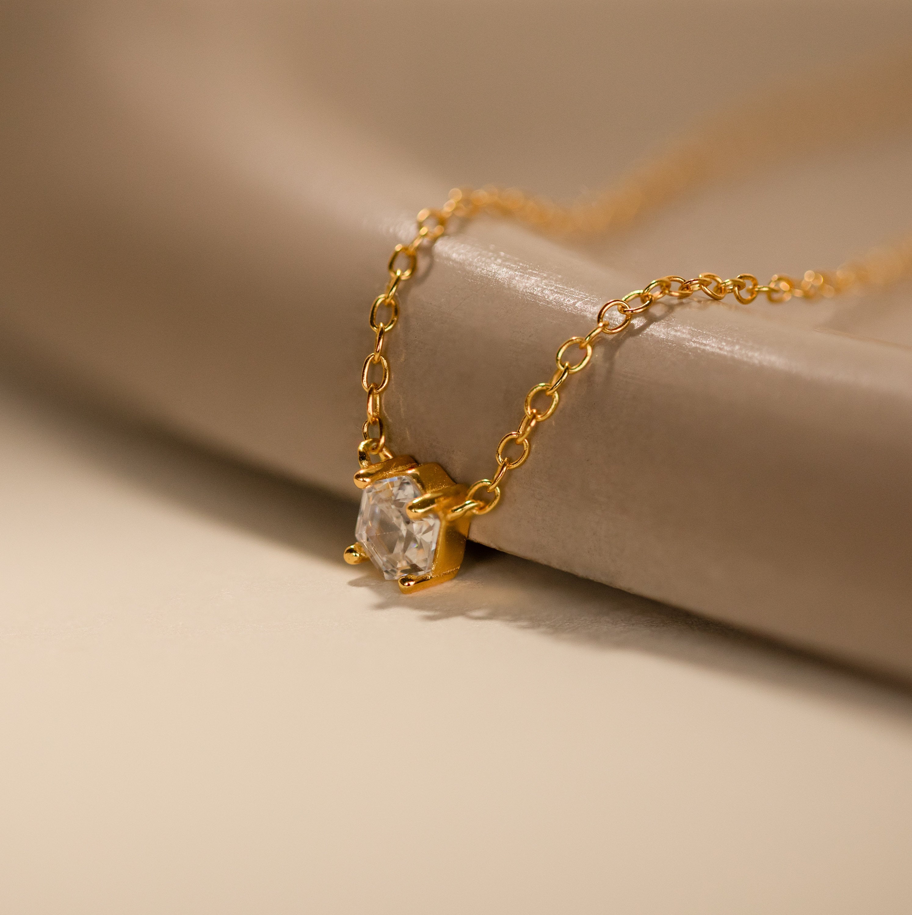 Hexagon Diamond Necklace featuring a rose-cut diamond pendant showcased on a smooth, beige surface.