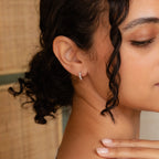 Close-up of a woman wearing Moonstone Huggies, her hand near her neck and curly hair framing the minimalist earrings.