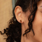 A close-up of a person wearing small gold Saturn-shaped studs paired with Herkimer Smoky Quartz Studs for a subtle celestial vibe.