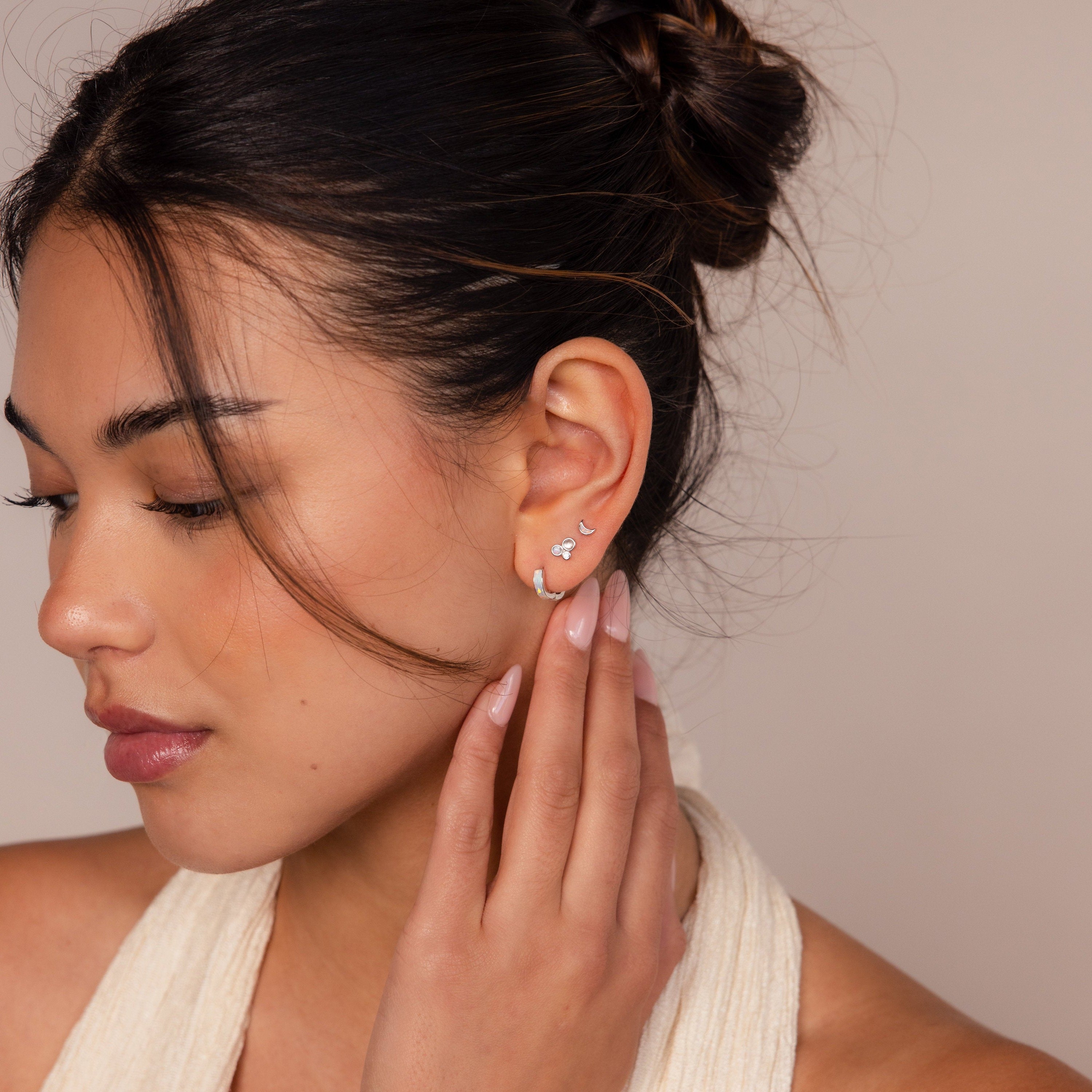 Woman with dark hair in a bun, gently touching her ear adorned with the Opal Inlay Earrings Set—featuring multiple small silver accents. A perfect jewelry set gift for her.