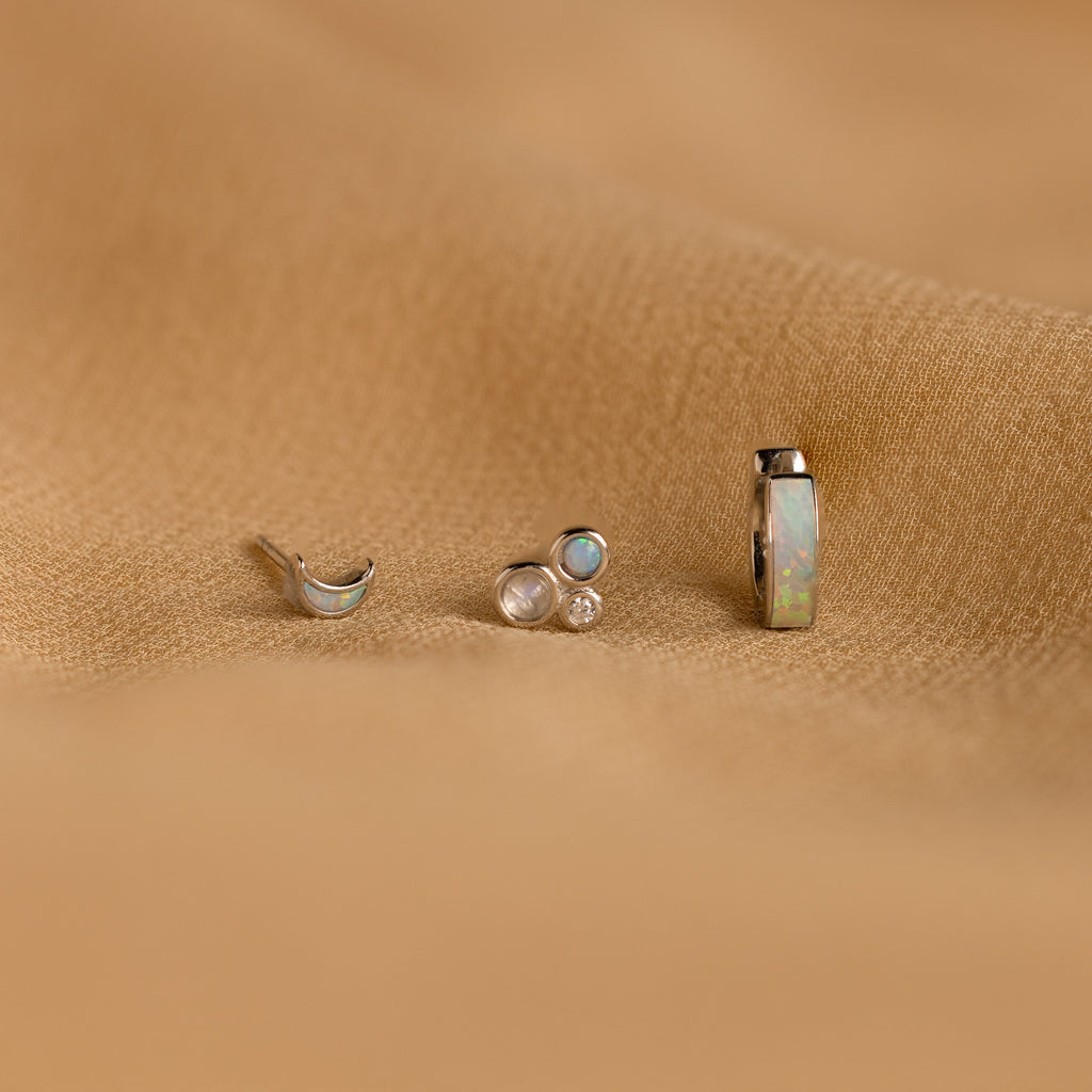 The Opal Inlay Earrings Set features three small earrings with gem settings, beautifully displayed on a textured light brown fabric—an eye-catching opal jewelry set and the perfect gift for her.