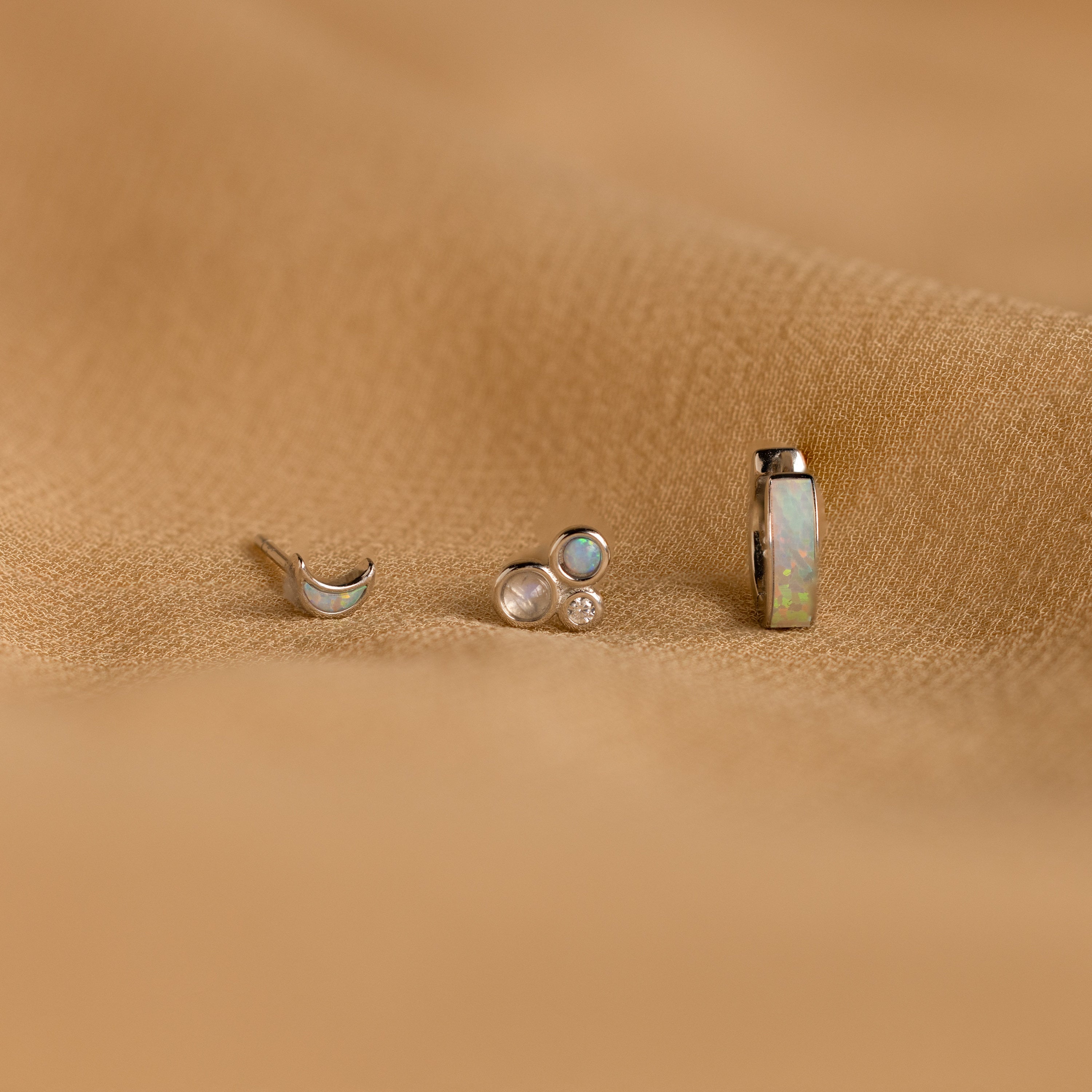 The Opal Inlay Earrings Set features three small earrings with gem settings, beautifully displayed on a textured light brown fabric—an eye-catching opal jewelry set and the perfect gift for her.