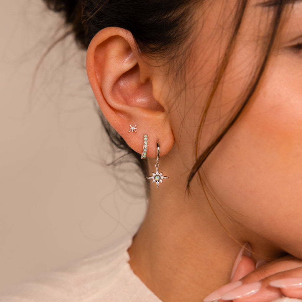 A woman's ear is adorned with the Opal Starburst Earrings Set, featuring a star-shaped dangly earring and two studs—ideal for mixing and matching with your favorite jewelry sets.