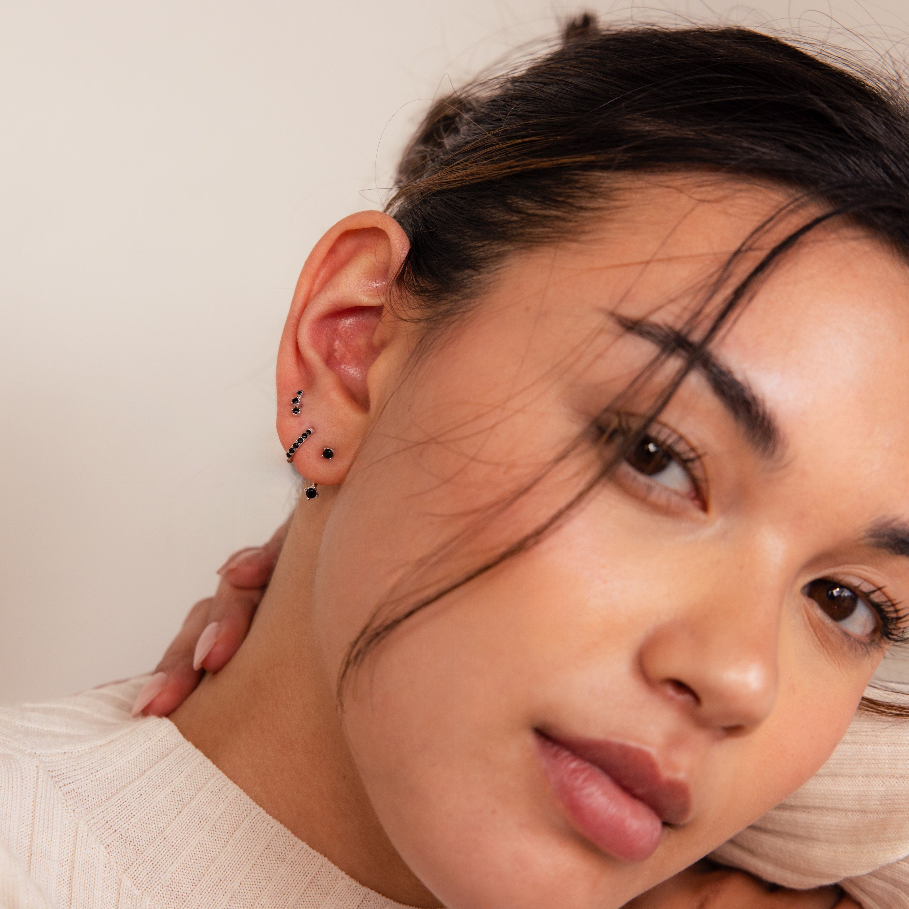 A woman with dark hair elegantly displays the Black Diamond Earrings Set along her ear, perfectly paired with a cream sweater.