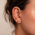 Close-up of a woman’s ear adorned with the Black Diamond Earrings Set, featuring gold and black stud and hoop earrings, including a chic climber stud and elegant gemstone huggie hoop.