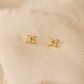 The Opal Ivy Flower Studs feature small gold flowers with four opal-like stones, displayed on soft cream fabric. These delicate earrings are a meaningful gift for any occasion.