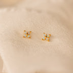 The Dainty Opal Stud Earrings Set features four small opal stones on gold settings, displayed against a soft cream fabric—ideal for those who love minimalist jewelry.