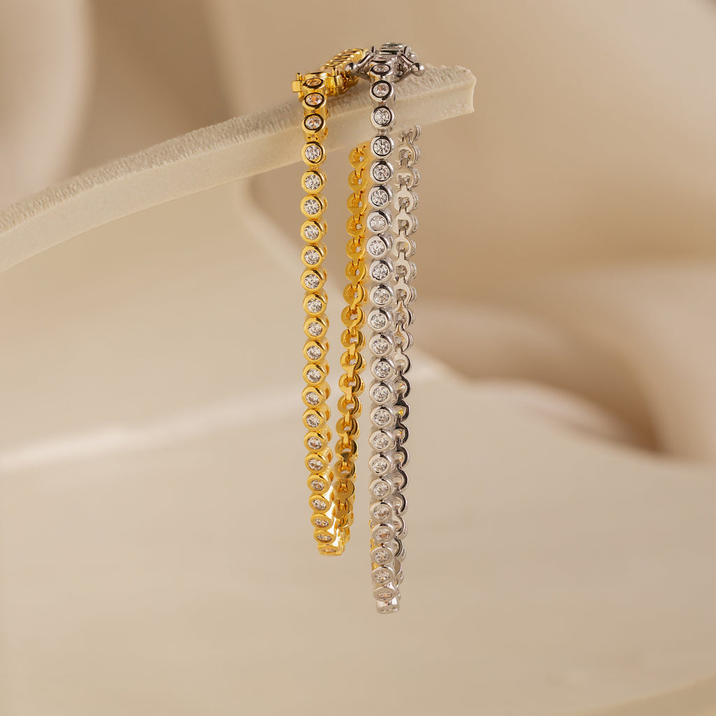 Diamond Bezel Tennis Bracelets in gold and silver with round diamonds are displayed on a soft beige background, making them the perfect personalized bridal gift.