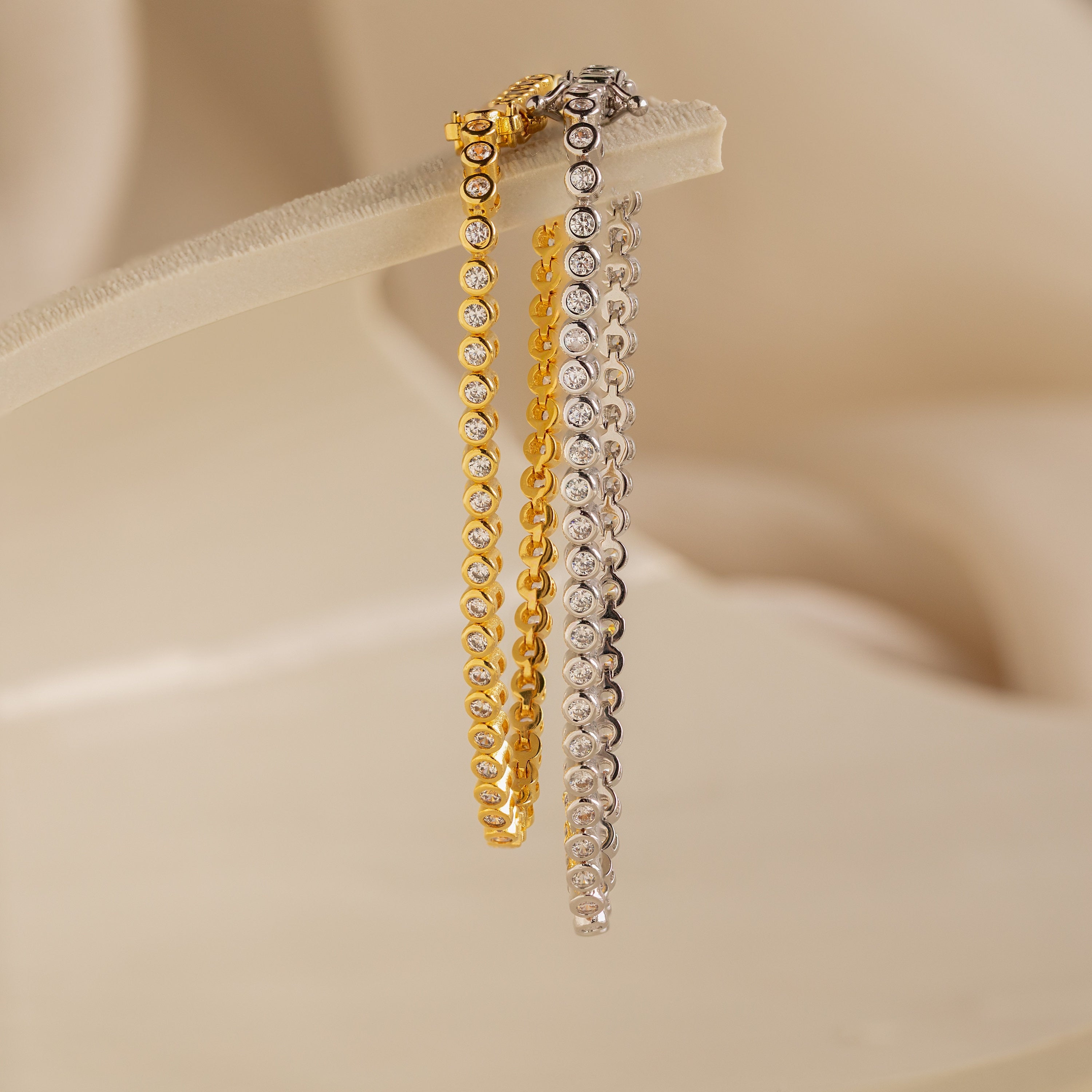 Diamond Bezel Tennis Bracelets in gold and silver with round diamonds are displayed on a soft beige background, making them the perfect personalized bridal gift.