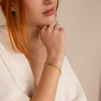A red-haired woman in a white top rests her chin on her hand, showcasing the elegant Emerald Baguette Tennis Bracelet—a standout piece of statement jewelry.