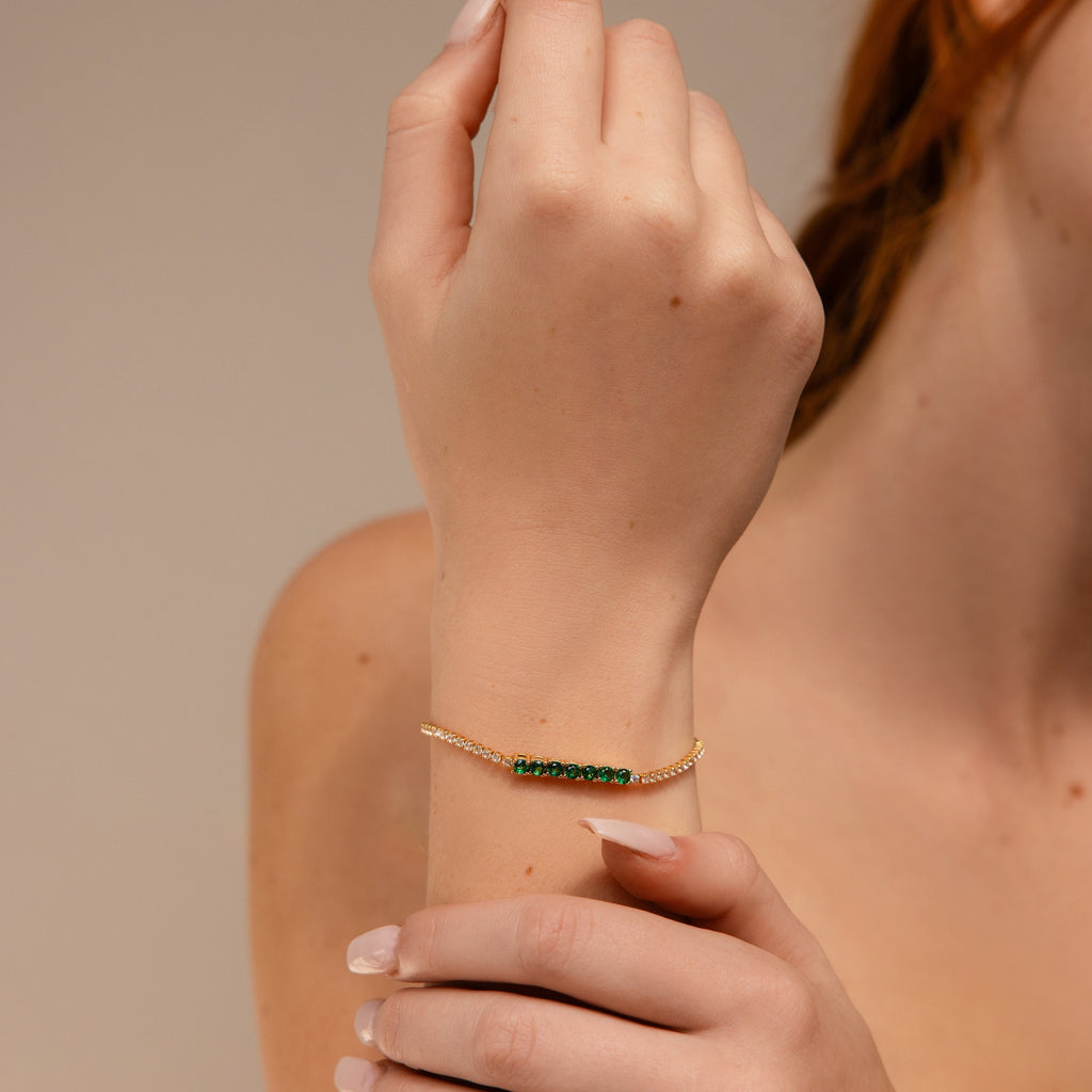 A person wearing an Emerald Diamond Tennis Bracelet with green beads raises their hand near their face.