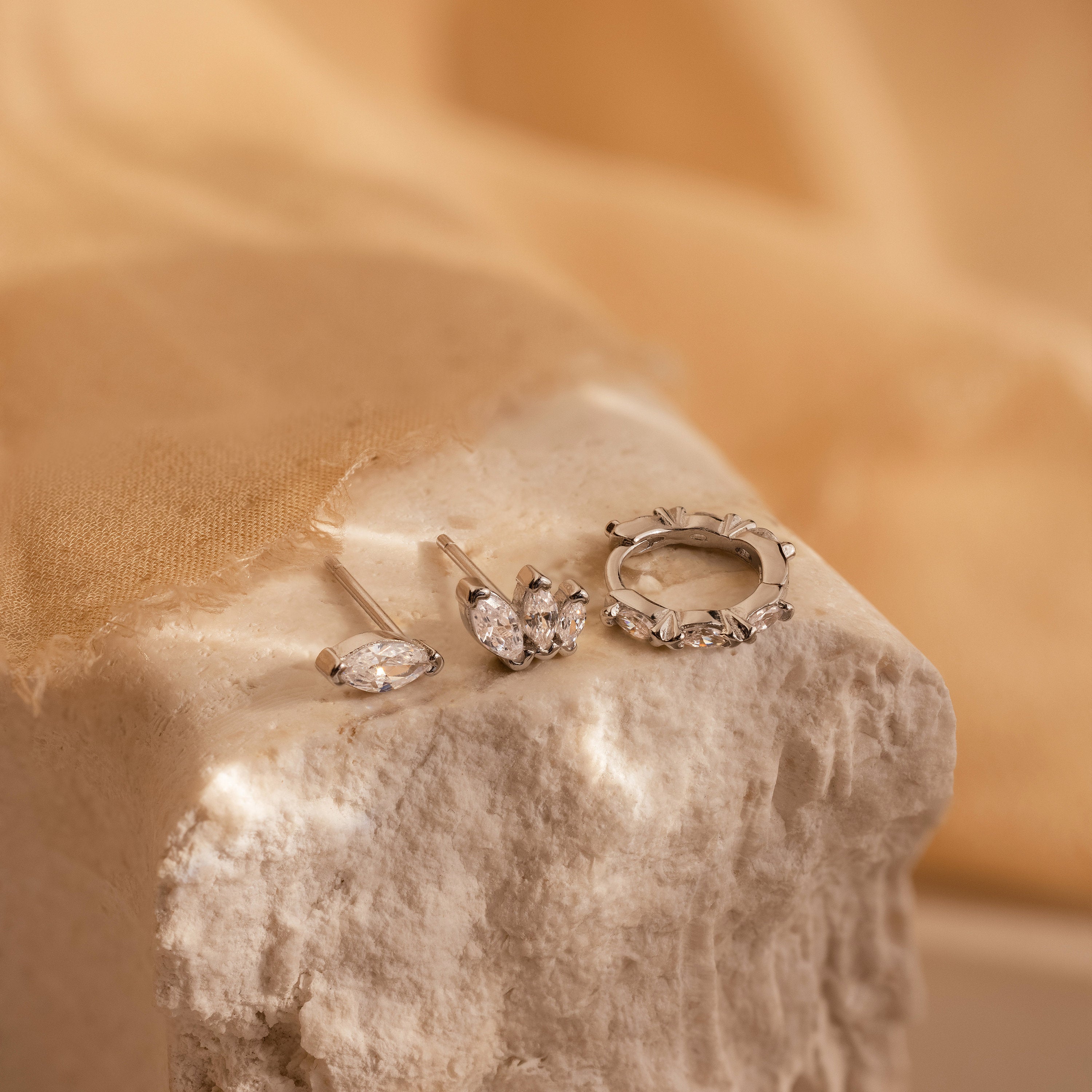 The Marquise Diamond Earrings Set features three silver marquise diamond earrings displayed on textured stone, evoking wedding elegance and making perfect bridesmaid gifts against a soft beige background.