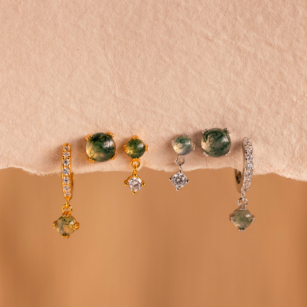 Four pairs of gemstone and diamond earrings, including the Agate Earrings Set, in gold and silver are displayed on a beige textured surface.