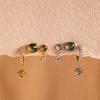 Four pairs of gemstone and diamond earrings, including the Agate Earrings Set, in gold and silver are displayed on a beige textured surface.