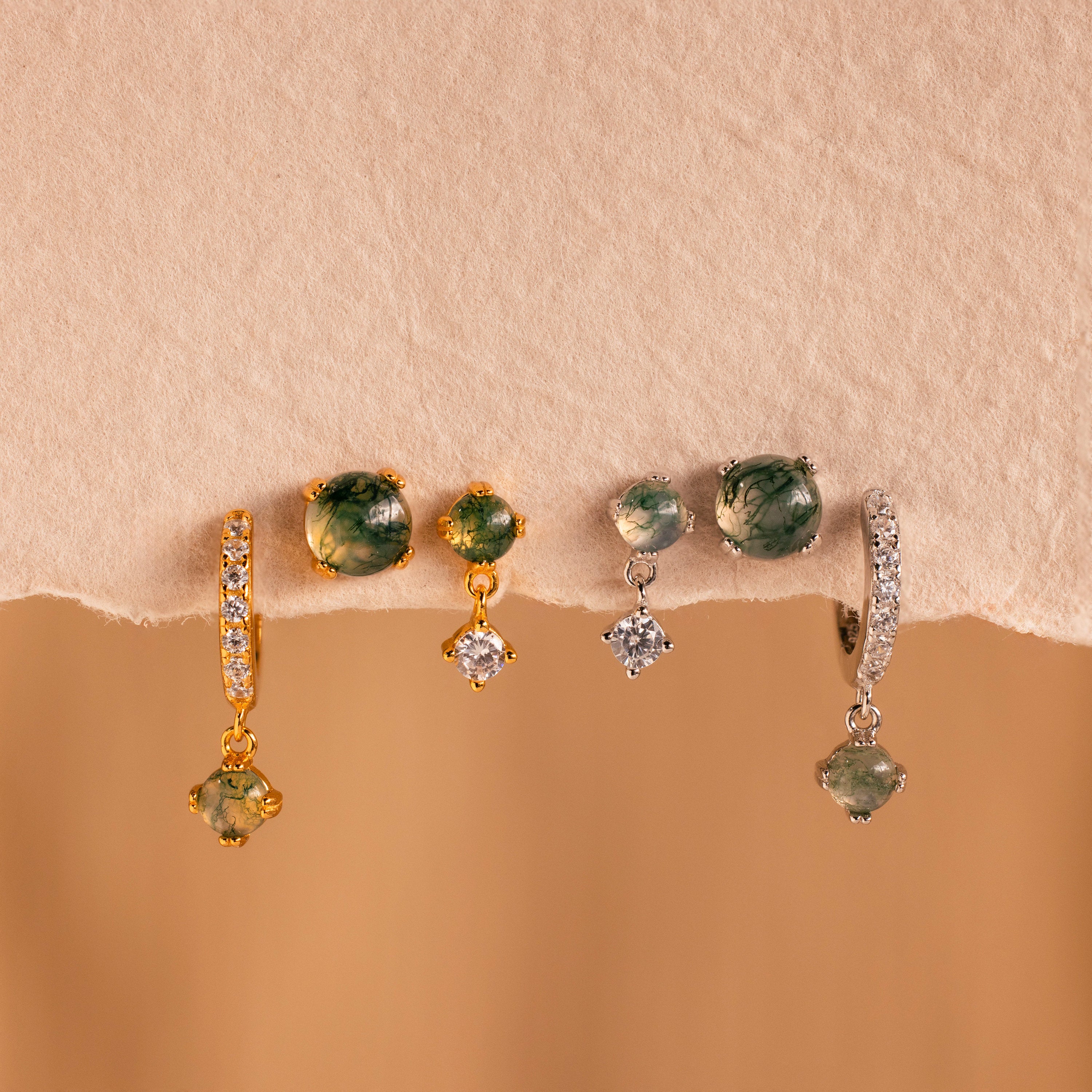 Four pairs of gemstone and diamond earrings, including the Agate Earrings Set, in gold and silver are displayed on a beige textured surface.