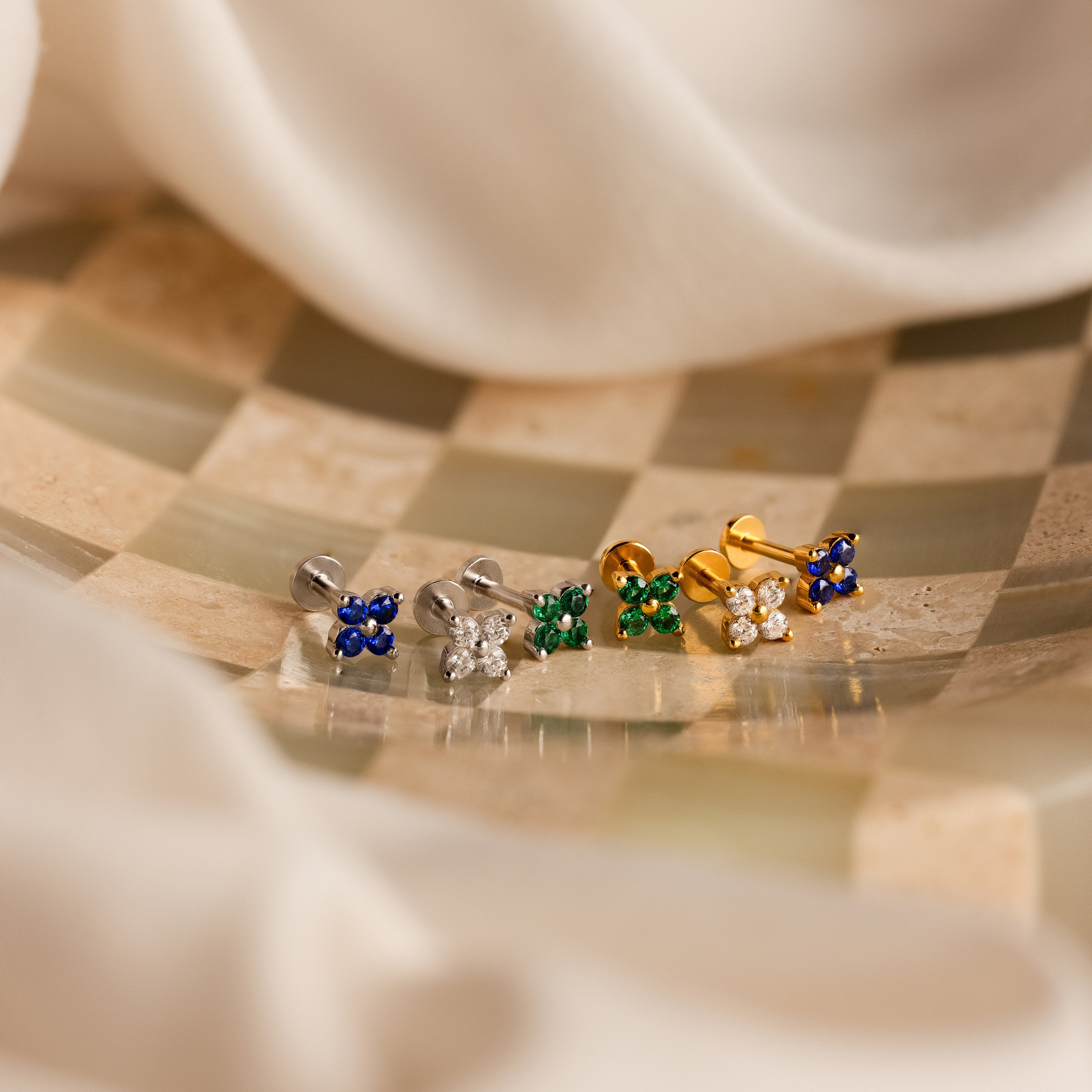 The Flower Flat Back Studs Set features five pairs of colorful floral stud earrings arranged on a checkered surface with a soft fabric backdrop, highlighting trendy nap earrings ideal for everyday wear.