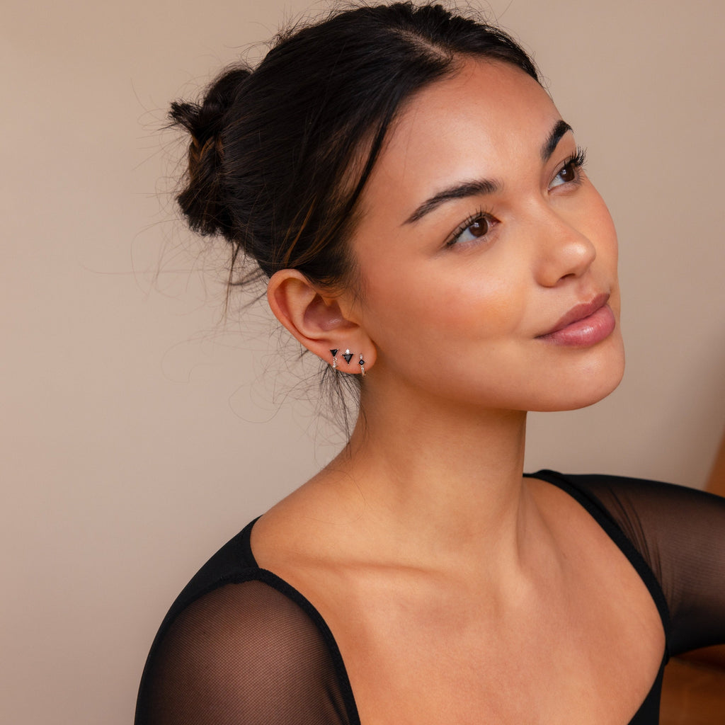 A woman with dark hair in a bun, wearing a black top and the Black Art Deco Earrings Set—minimalist geometric jewelry—gazes upward thoughtfully.