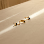 The Black Art Deco Earrings Set, featuring geometric shapes and black stones, rests on beige fabric in sunlight—a striking example of minimalist jewelry.