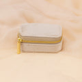 The Mini Travel Jewelry Box in beige velvet, featuring a gold zipper, is displayed on a matching soft fabric background.