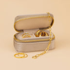 The Mini Travel Jewelry Box in beige, shown with gold rings and a chain on a neutral backdrop, is the perfect sleek organizer for your jewelry on trips.
