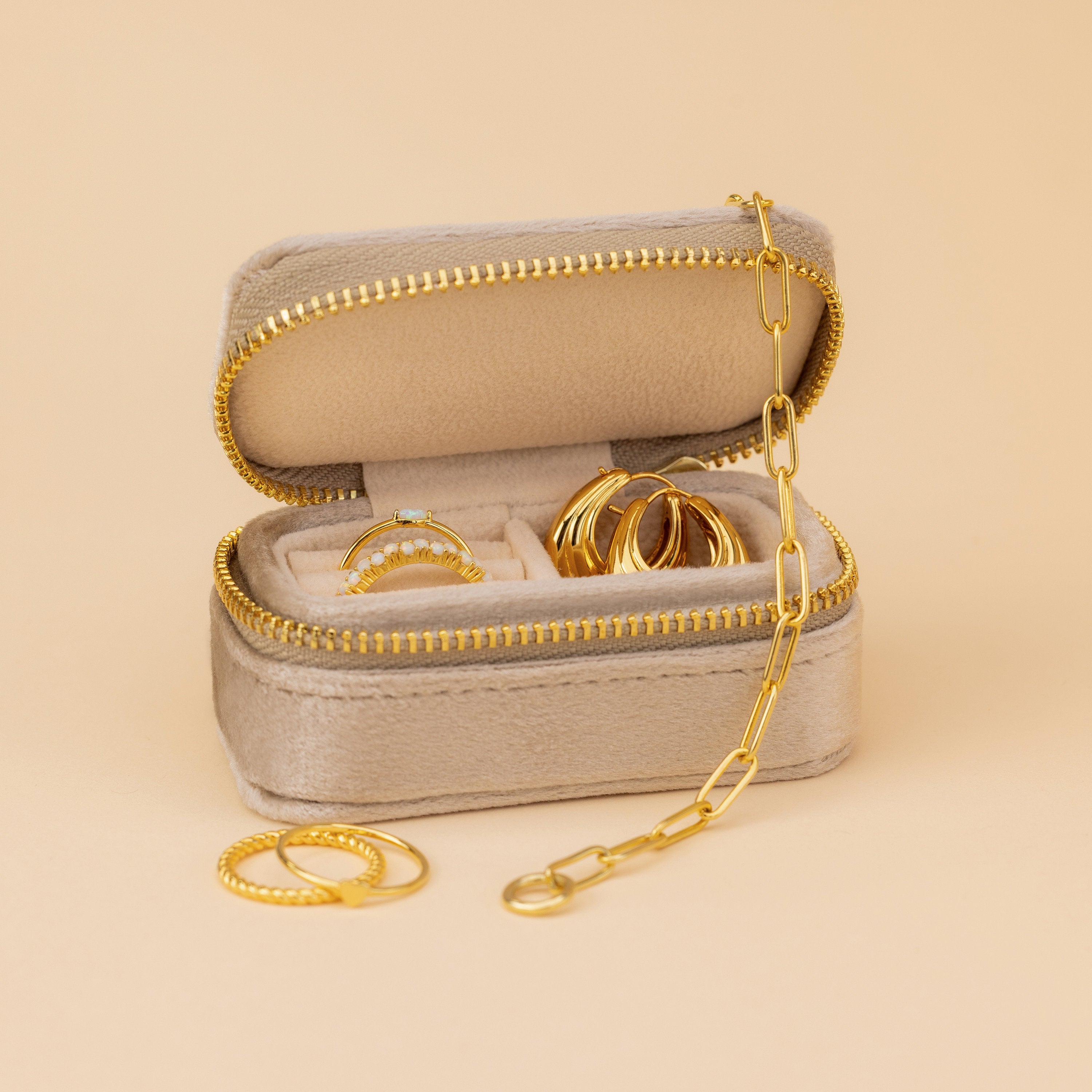 The Mini Travel Jewelry Box in beige, shown with gold rings and a chain on a neutral backdrop, is the perfect sleek organizer for your jewelry on trips.