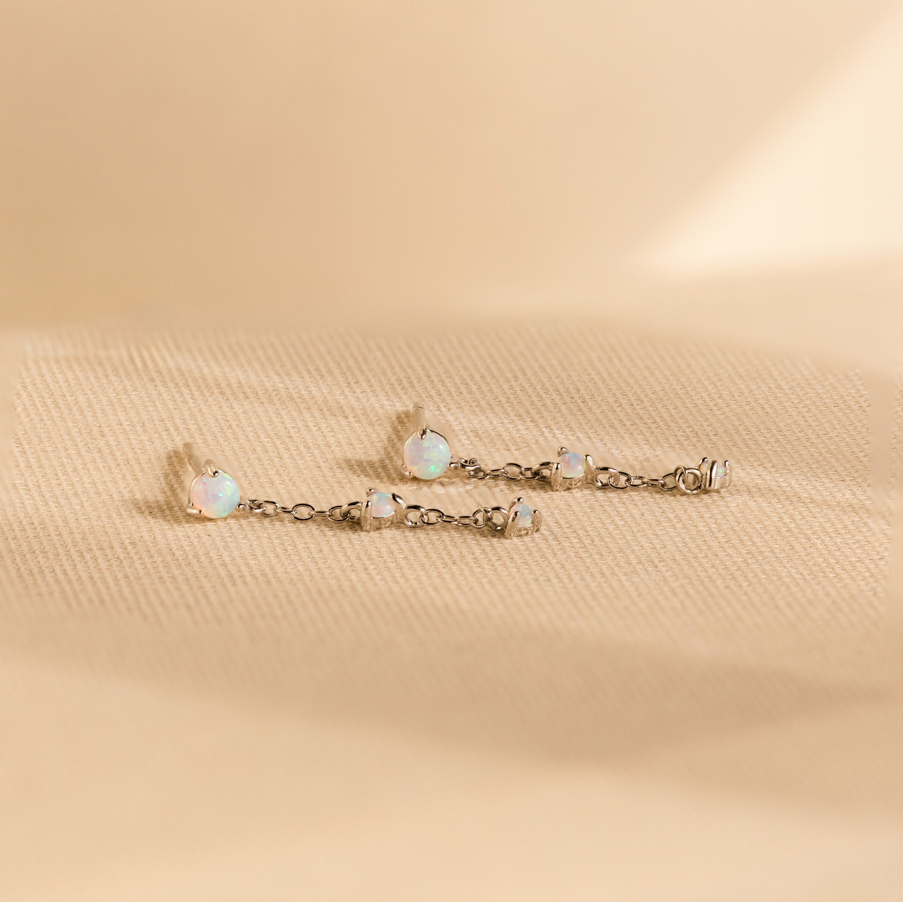 Opal Chain Drop Earrings—delicate silver chains shown on textured beige fabric—make the perfect elegant bridesmaid earrings for special occasions.