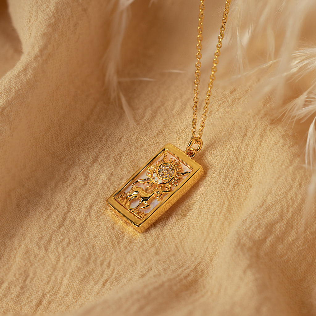 The Sun & Moon Tarot Necklace is displayed on soft beige fabric with white feathery accents, making it a perfect statement jewelry piece.