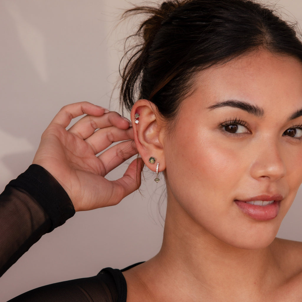 A woman with dark hair in a bun touches her ear, highlighting the Agate Earrings Set. Wearing a black top and smiling softly, she showcases the elegance of this jewelry.