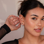 A woman with dark hair in a bun touches her ear, highlighting the Agate Earrings Set. Wearing a black top and smiling softly, she showcases the elegance of this jewelry.