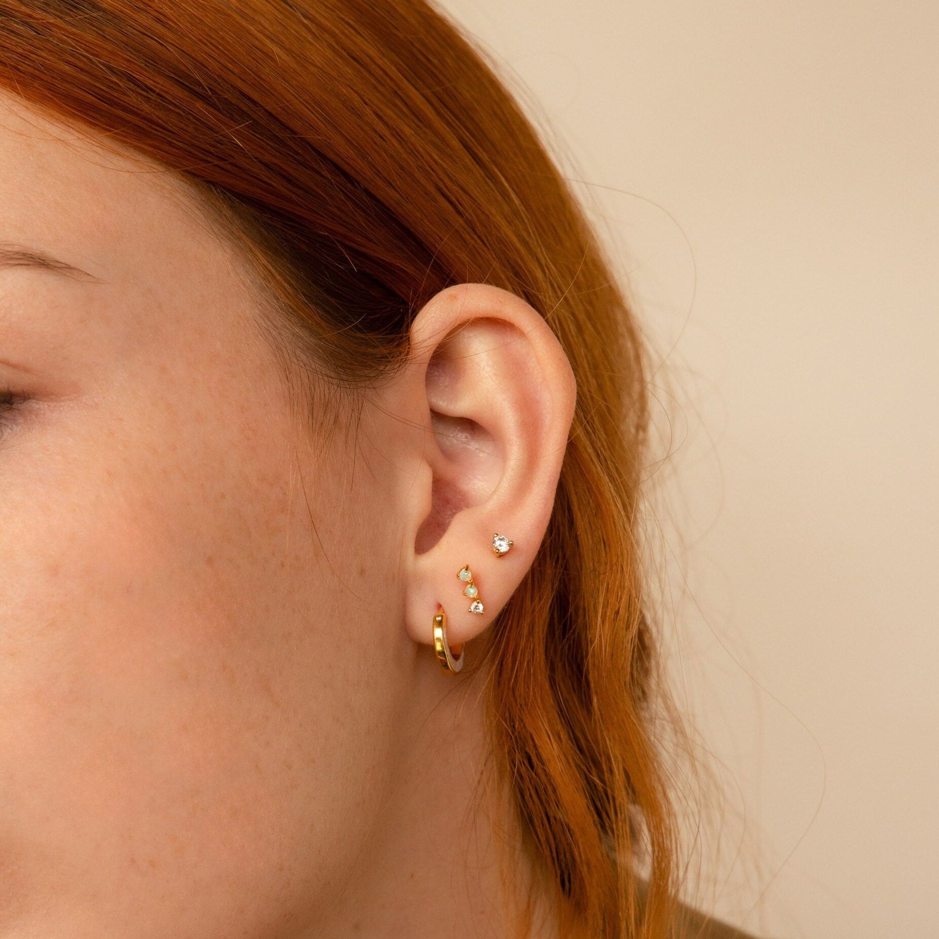 Close-up of a person's ear wearing Opal Diamond Bar Studs and a gold hoop earring, with hints of red hair.