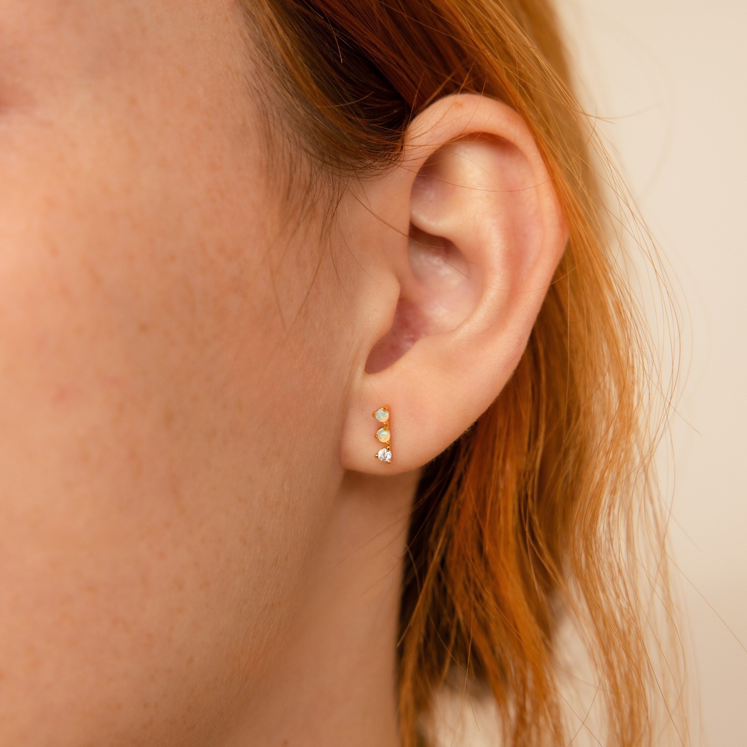 Close-up of a person's ear with three gold stud earrings—including Opal Diamond Bar Studs—delicately arranged in a vertical row on the earlobe.