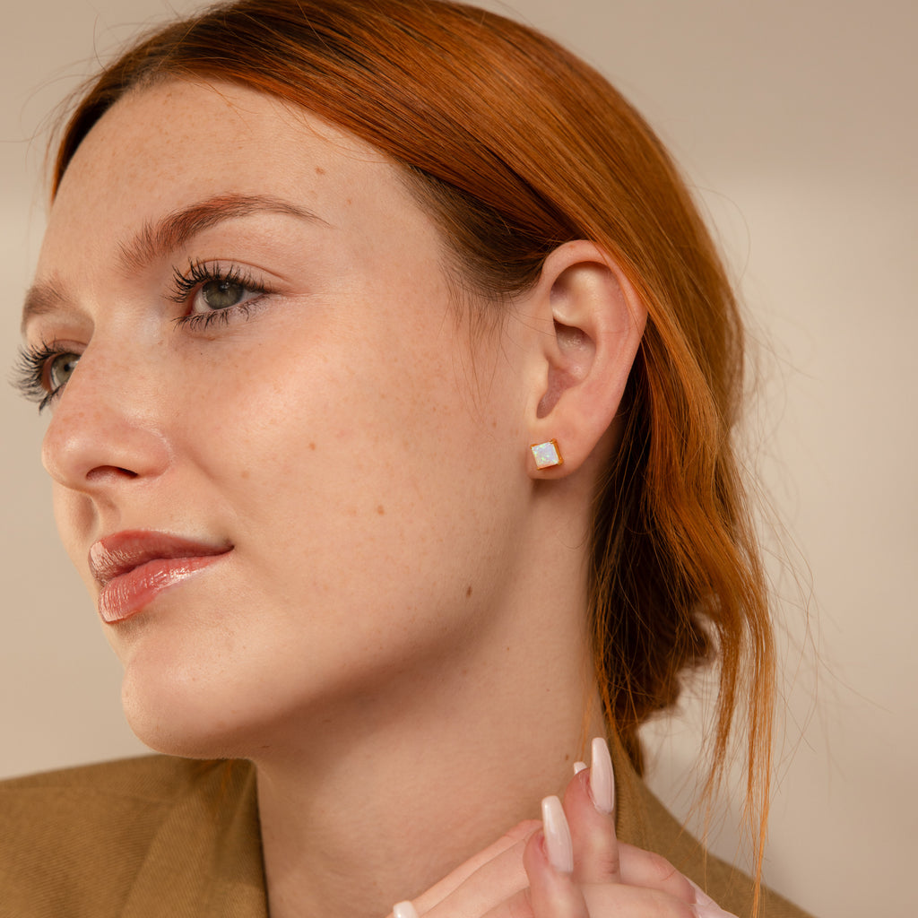 Red-haired woman in a beige blazer wears Princess Cut Opal Studs, gazing thoughtfully to the side.